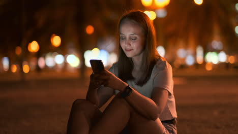 Ein-Schönes-Junges-Mädchen-Im-Sommer-In-Einer-Großen-Nachtstadt-Hält-Ein-Smartphone-In-Der-Hülle-Und-Schreibt-Eine-Nachricht,-Liest-E-Mails-Und-Kommuniziert-In-Chatrooms-Und-Sozialen-Netzwerken,-Führt-Einen-Blog-Und-Schaut-Auf-Den-Telefonbildschirm